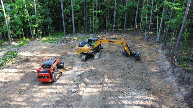 An aerial view of two excavators working in a dirt field in the woods.