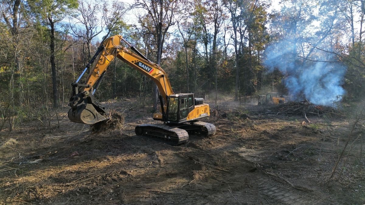A yellow excavator is digging a hole in the middle of a forest.