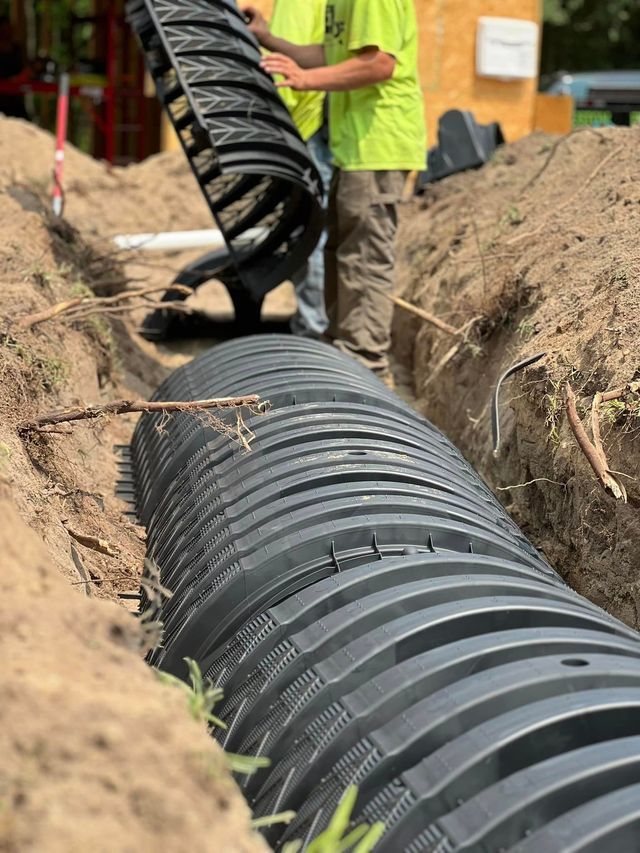 Two men are working on a septic system in a trench.