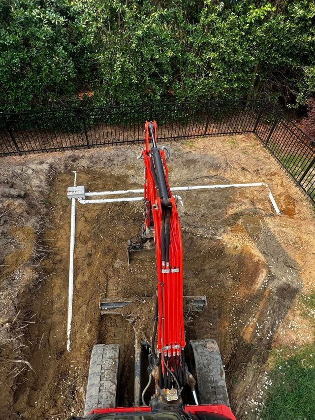 A red excavator is digging a hole in the ground in a backyard.