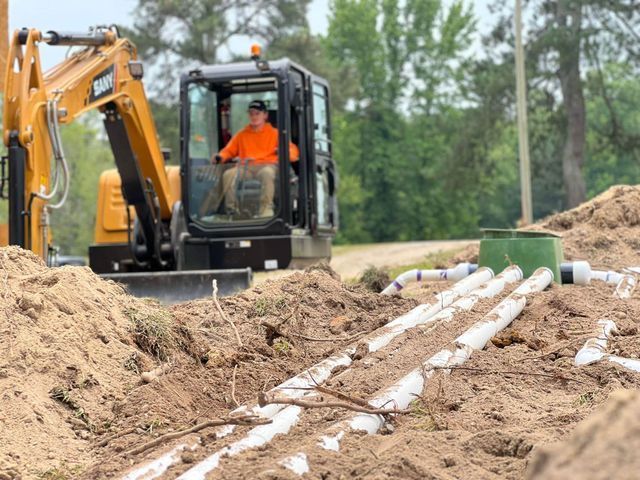 A man is driving an excavator in a dirt field.