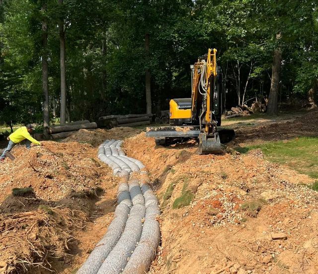 A yellow excavator is working on a drainage system in the dirt.