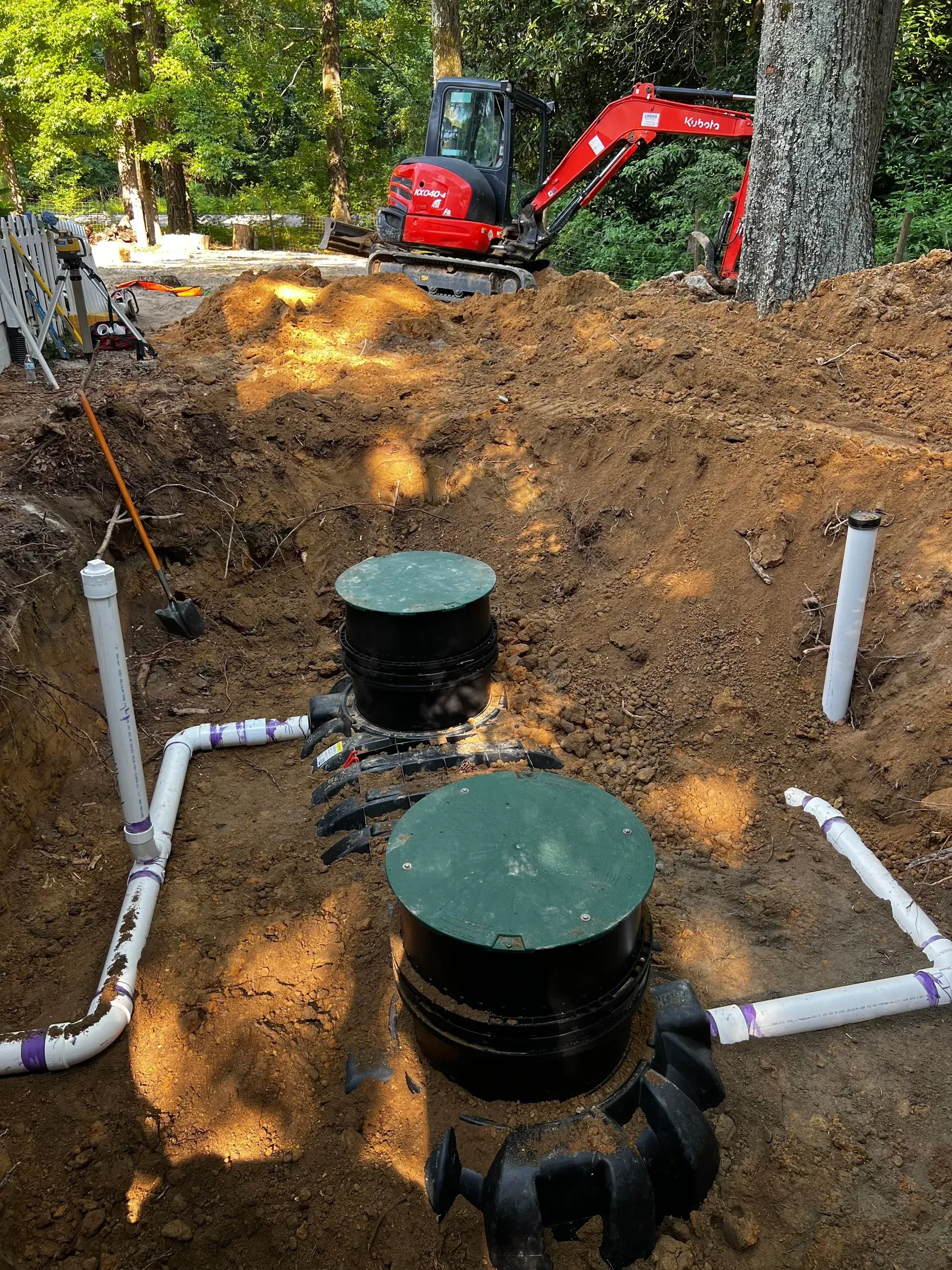 A septic system is being installed in a backyard with a red excavator in the background.