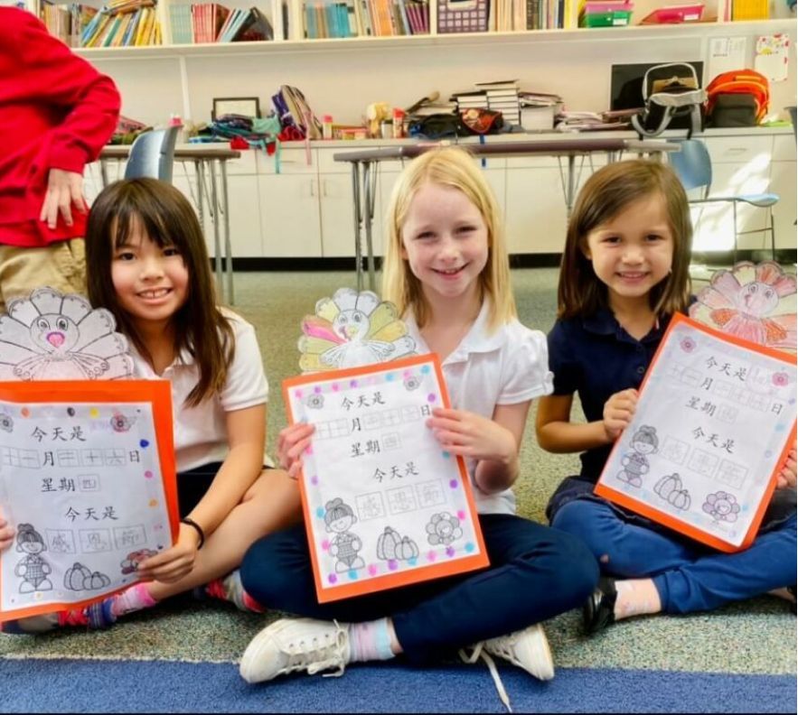 Three young girls are sitting on the floor holding papers with chinese writing on them.