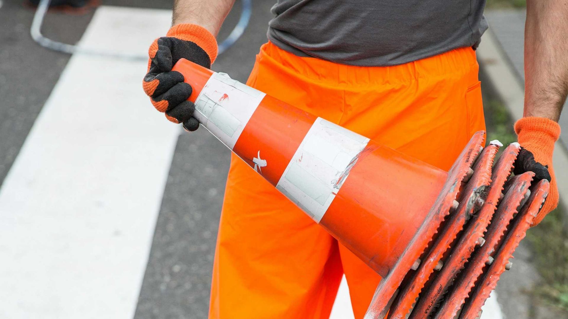 A man in orange pants and gloves is holding a traffic cone.