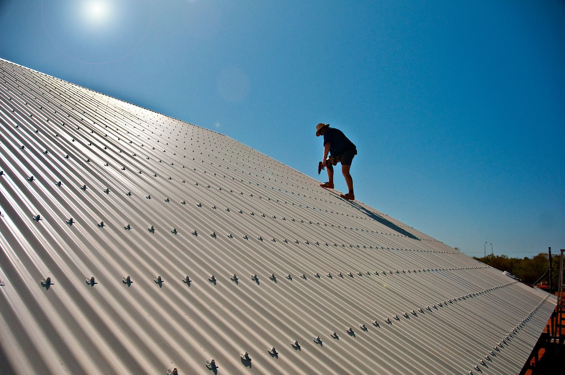 Person working on a metal roof under a clear blue sky.