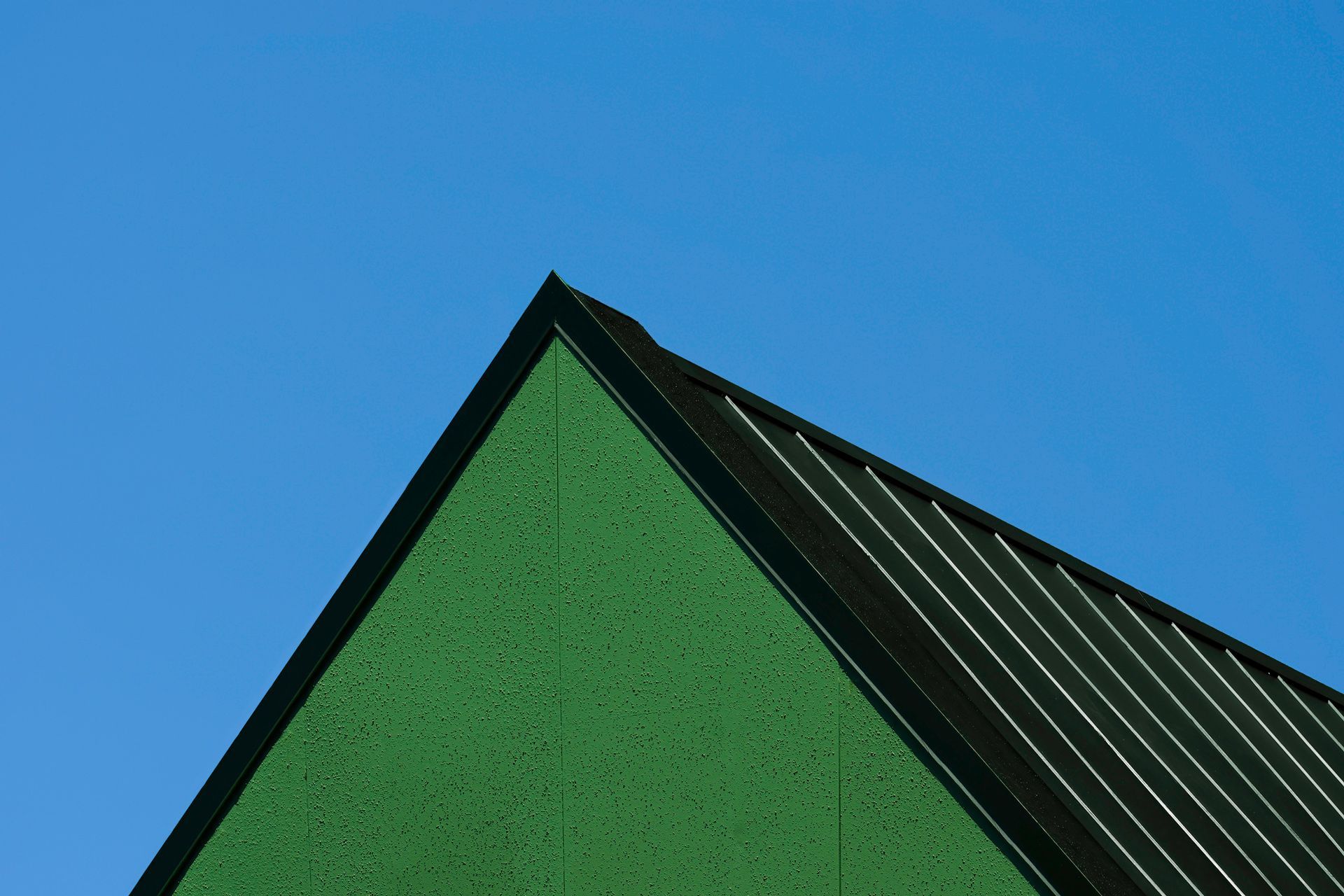 Green building corner against a blue sky, metal roof.