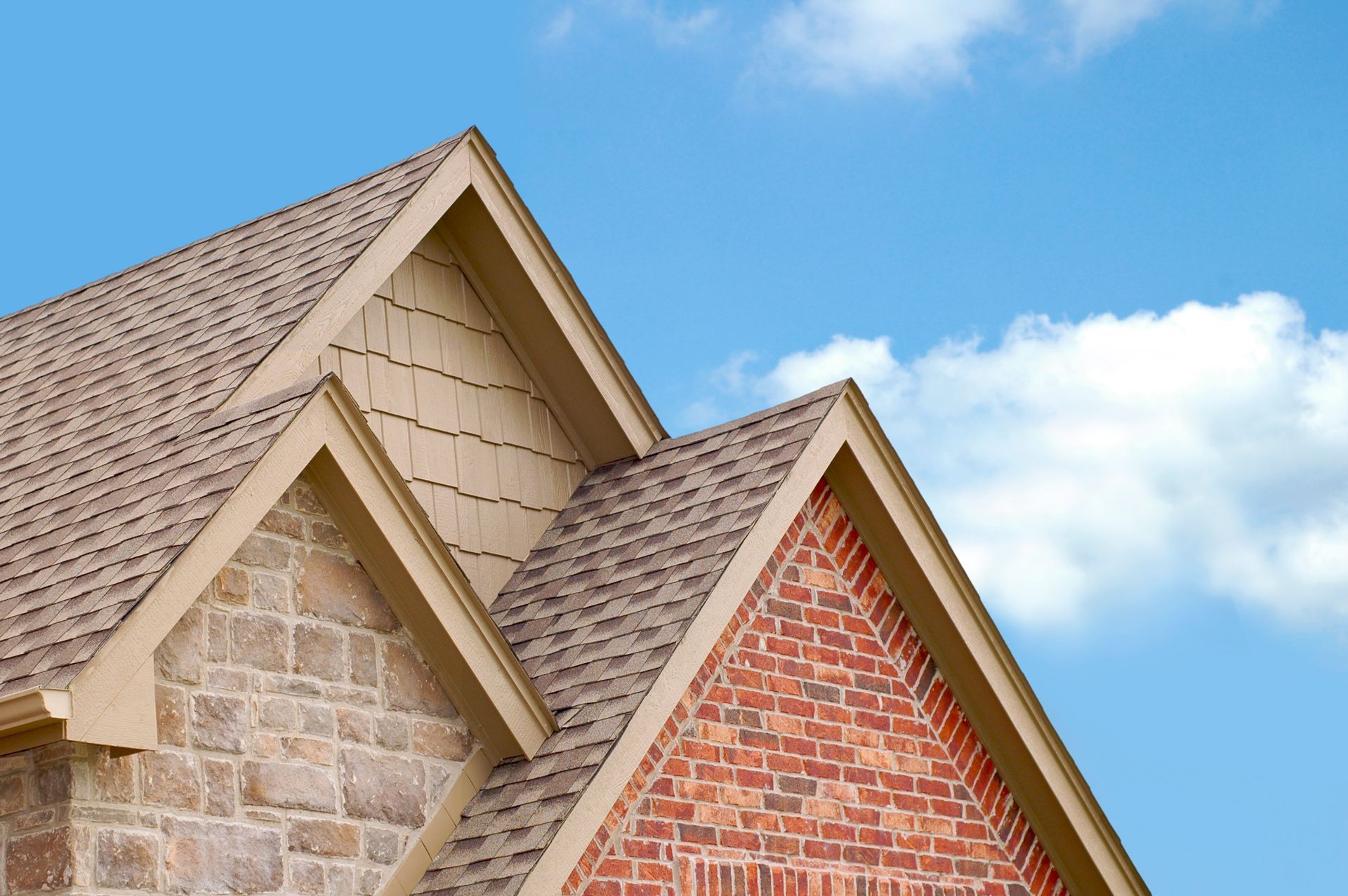 House roof with brick and stone siding, beige trim, and a blue sky.