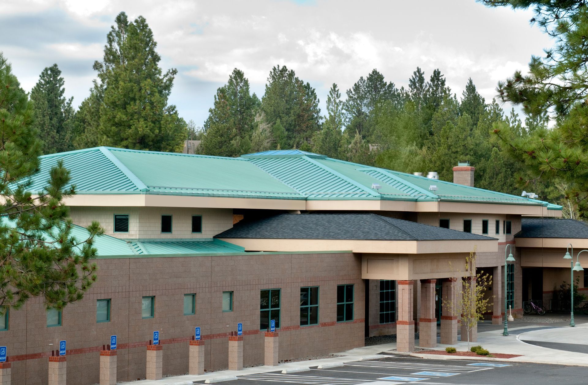 Building with green roof and brick facade, surrounded by trees and parking spaces.