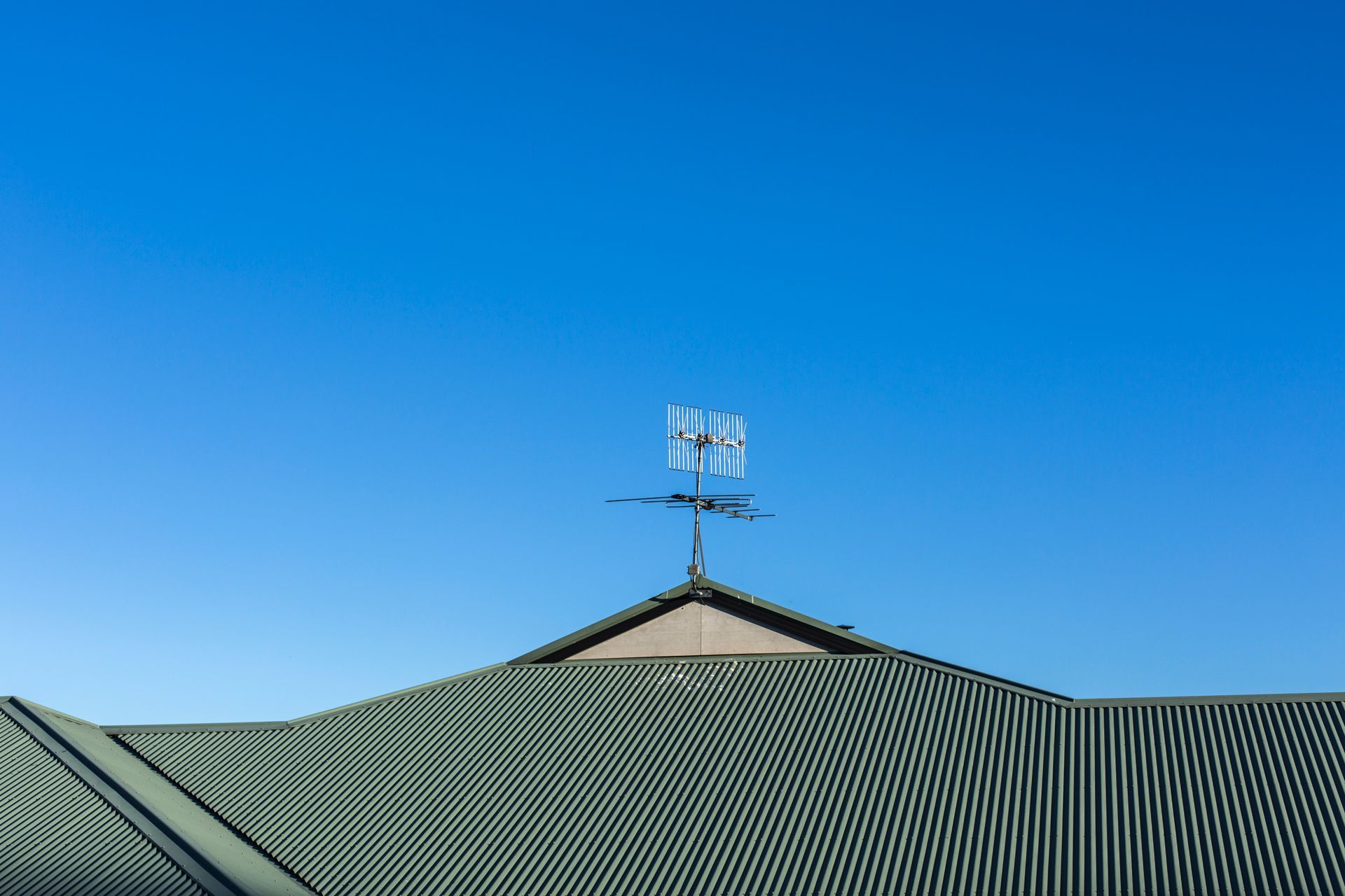 A rooftop with an antenna against a clear blue sky. Green, corrugated roof panels.