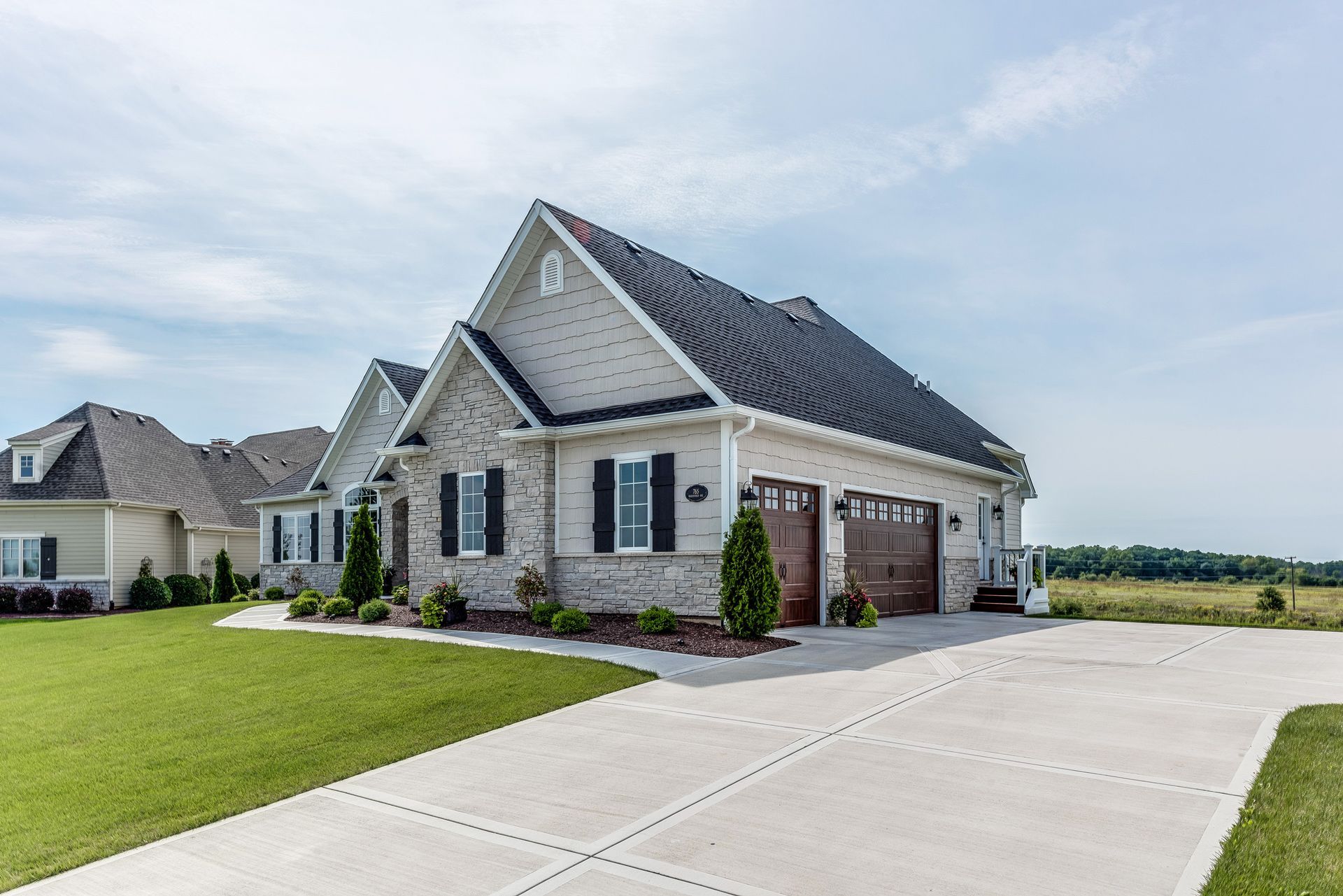 A light brick house with a dark roof and two-car garage under a blue sky, concrete driveway.