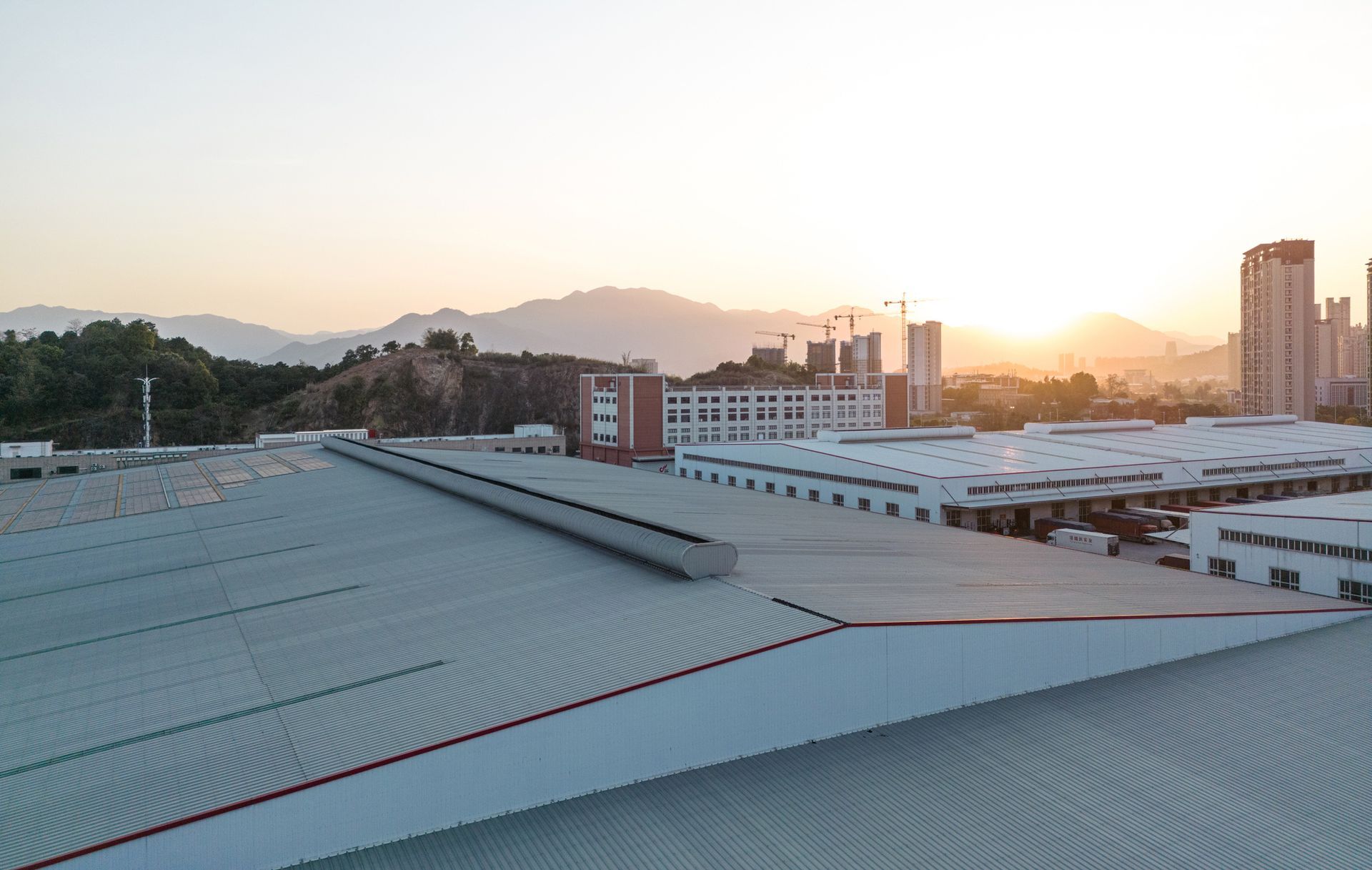 Industrial buildings with corrugated roofs, mountains, and a sunset in the background.