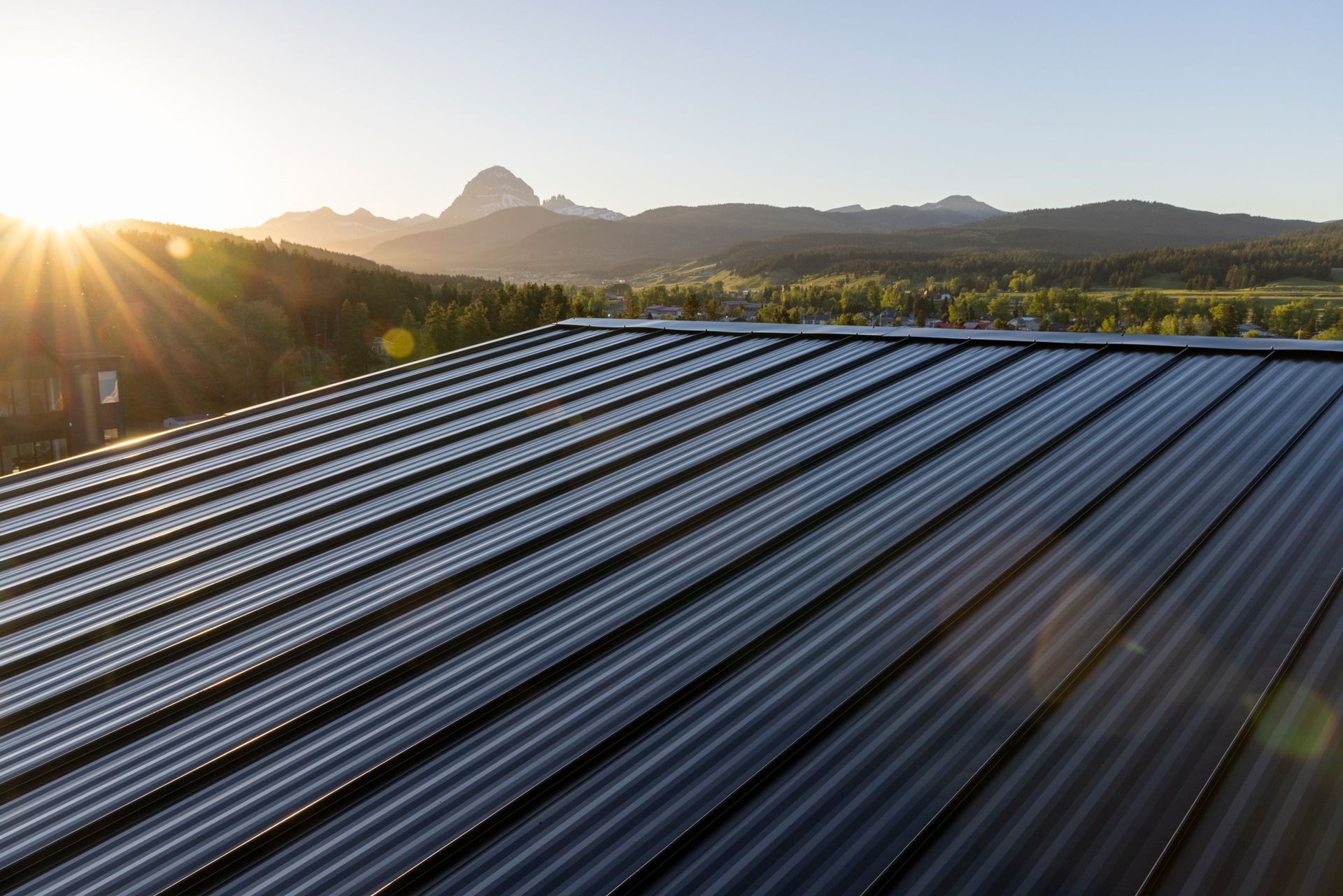 Solar panels on a roof, mountains and sun in the background.