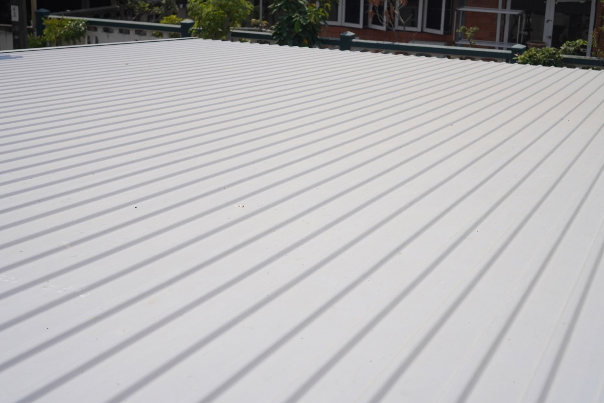 White roof with long shadows cast by the sun, building and trees visible in background.