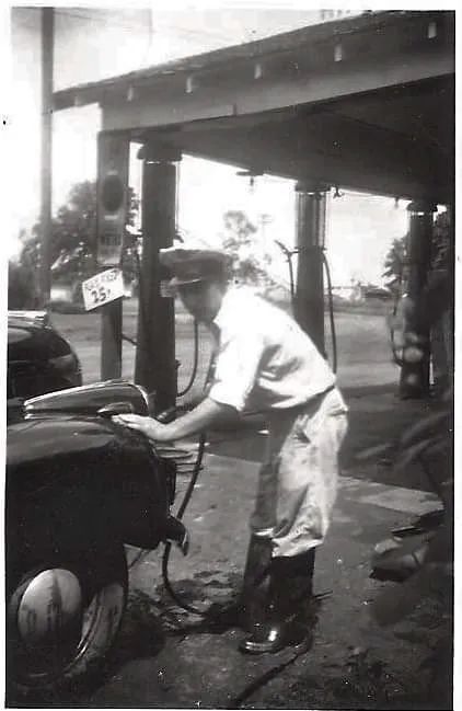 A black and white photo of a man pumping gas into a car.