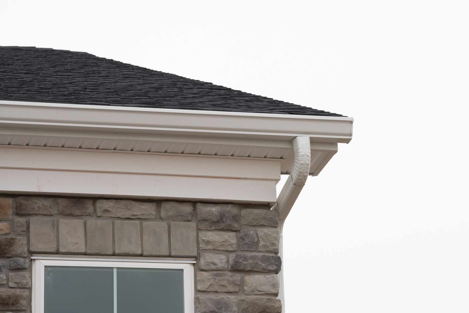 Close-up of a house roofline with white trim, stone exterior, and a window below.