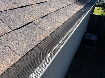 Close-up of a shingle roof with black gutter guards installed over a white gutter. Close-up of a shingle roof with black gutter guards installed over a white gutter.