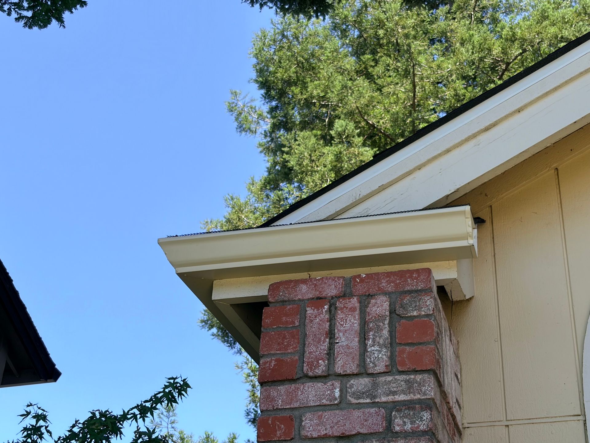 White seamless rain gutter installed above a brick column on a residential roof. White seamless rain gutter installed above a brick column on a residential roof.