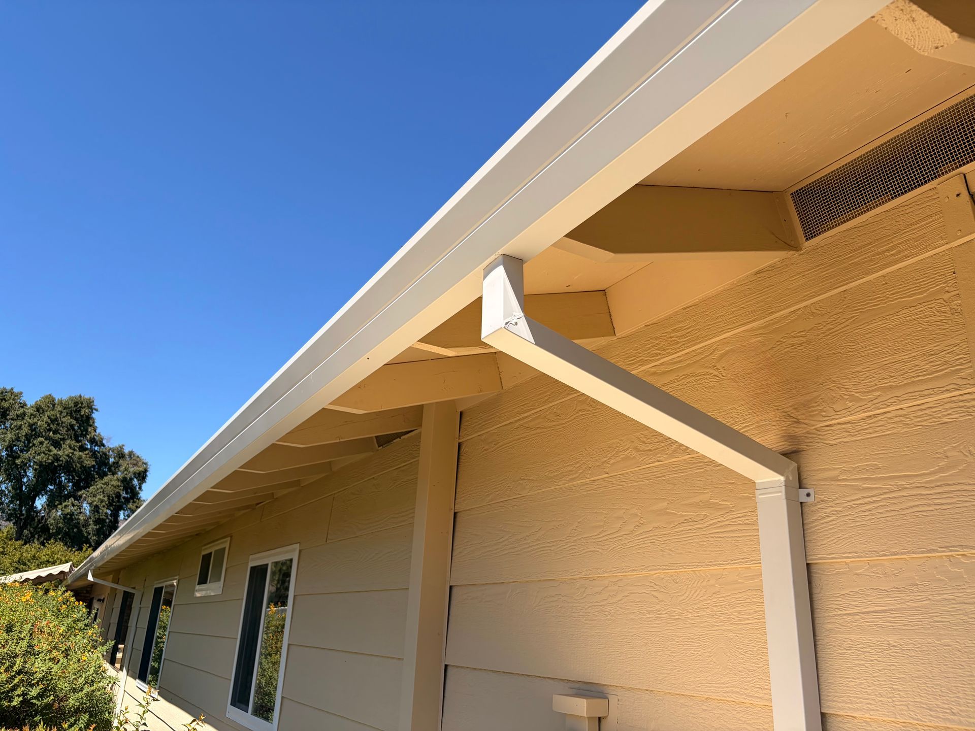 White aluminum rain gutter installed along the roof edge of a beige house exterior. White aluminum rain gutter installed along the roof edge of a beige house exterior.