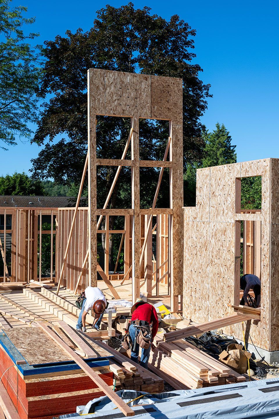 Construction work crew building a new house in a residential neighborhood, wood framing started, sunny summer construction season