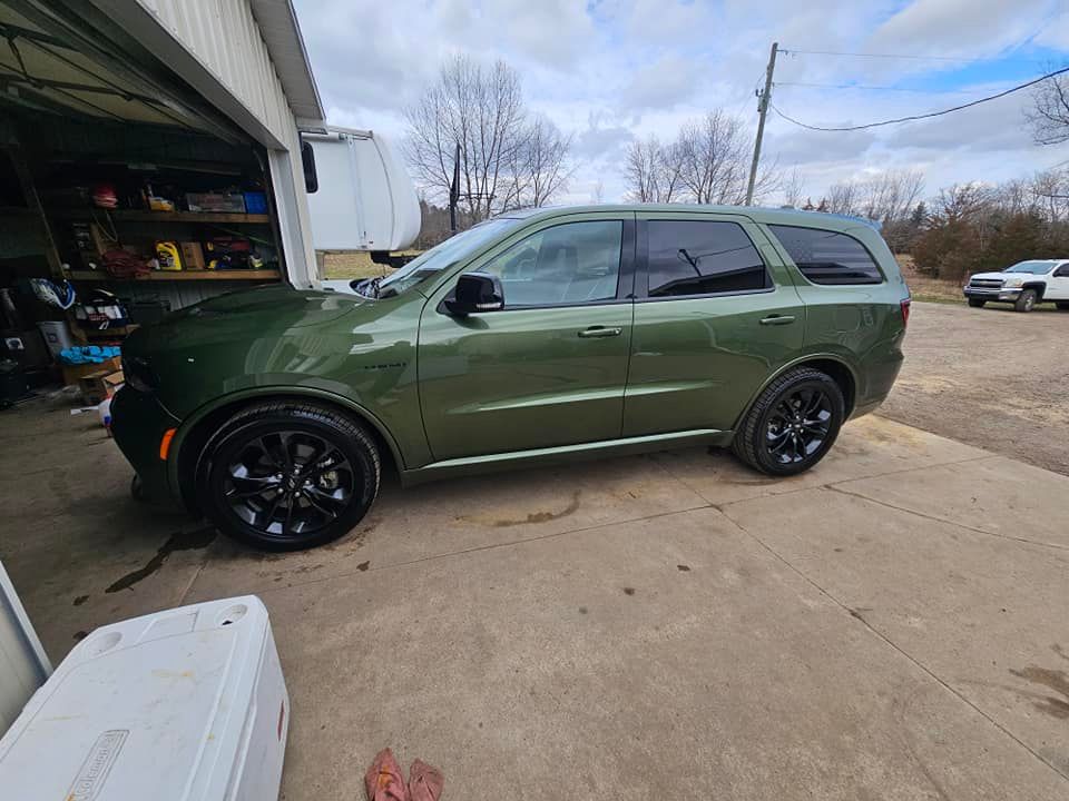 Green Dodge Durango SUV with black wheels parked in front of a garage.
