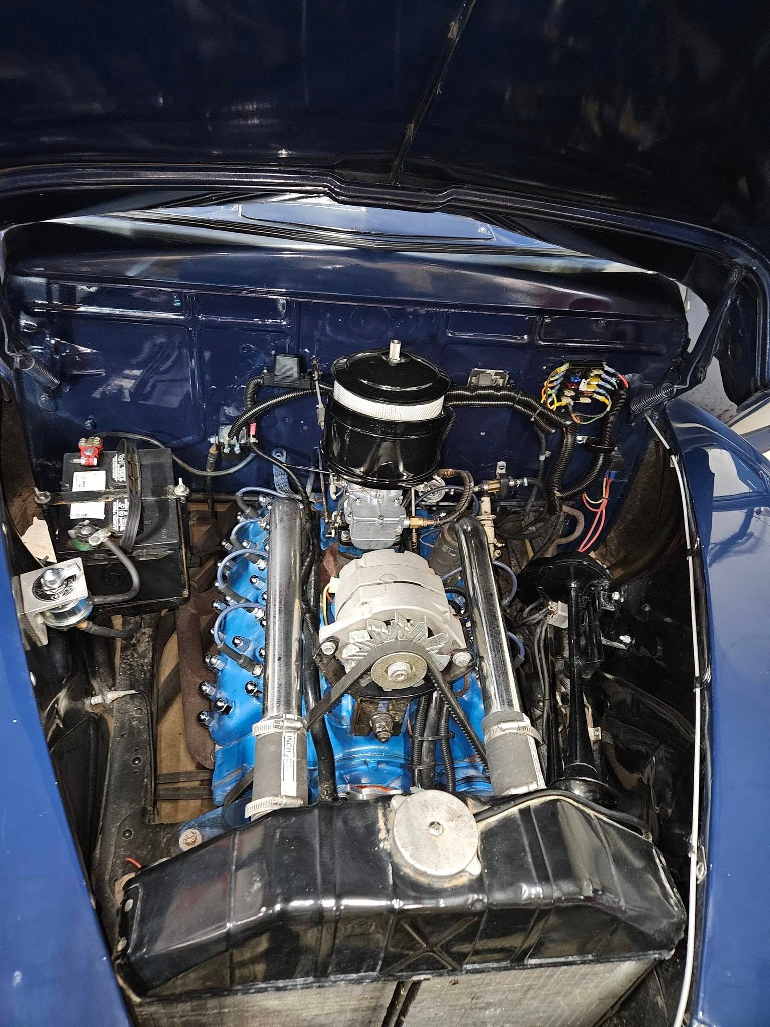 Blue car engine, black and blue components, in a dark blue engine bay.