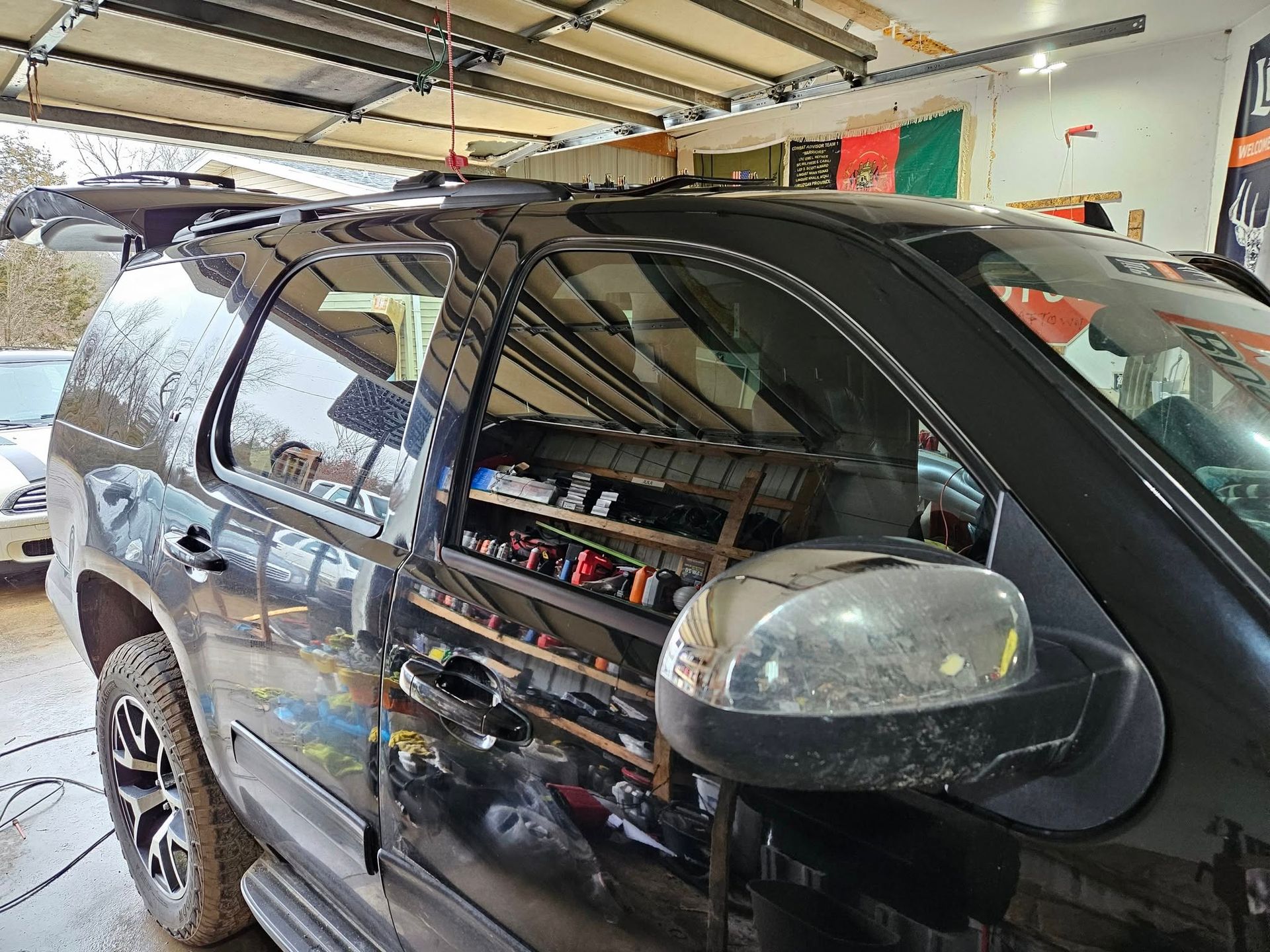 Black SUV parked in a garage with open garage door. Side view showing mirror and tinted windows.