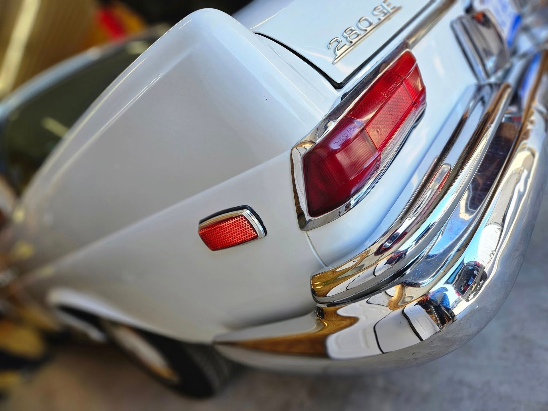 White classic car rear detail, chrome bumper, red taillight.