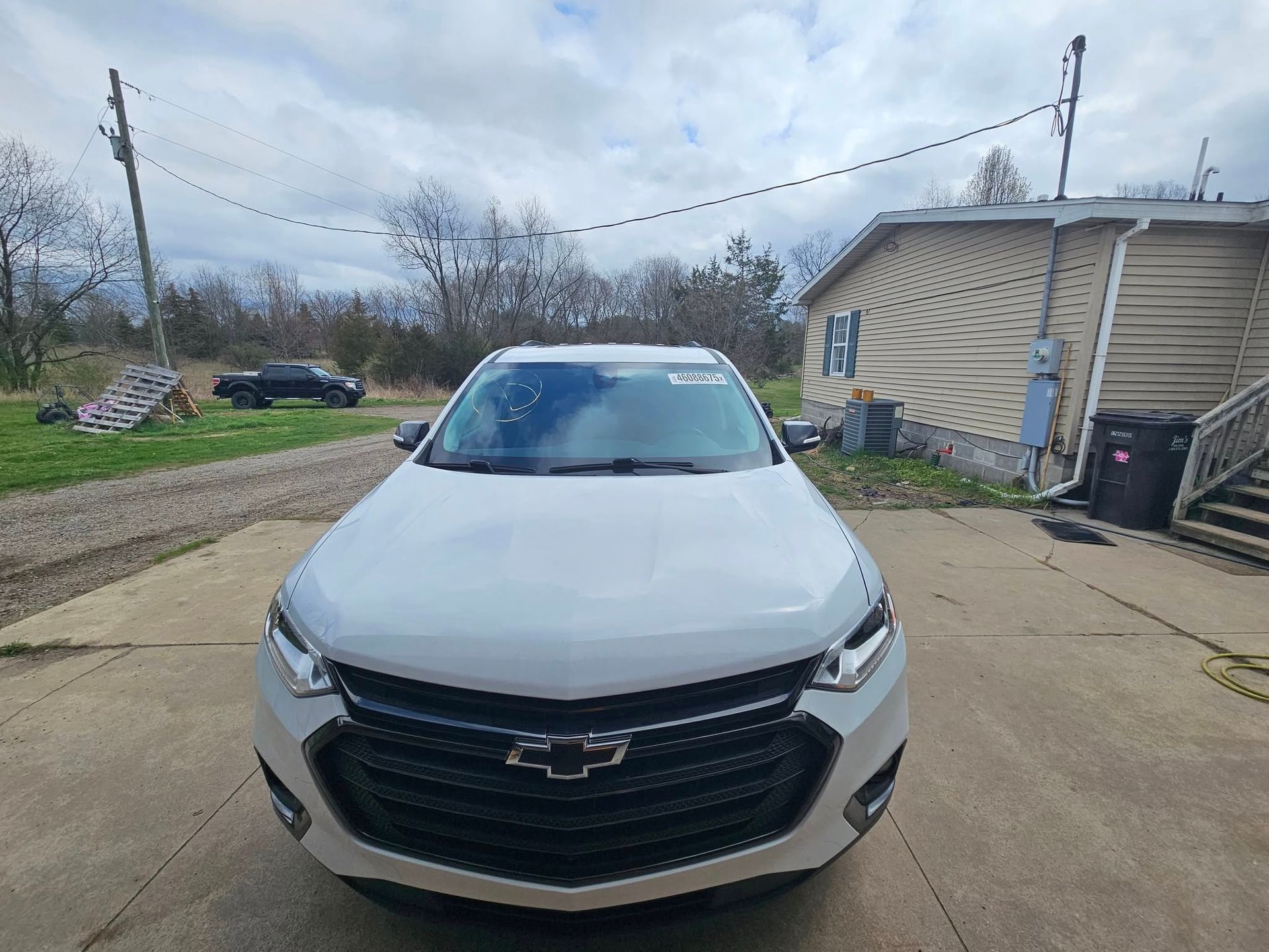 White Chevrolet SUV parked in front of a house. Cloudy sky overhead.