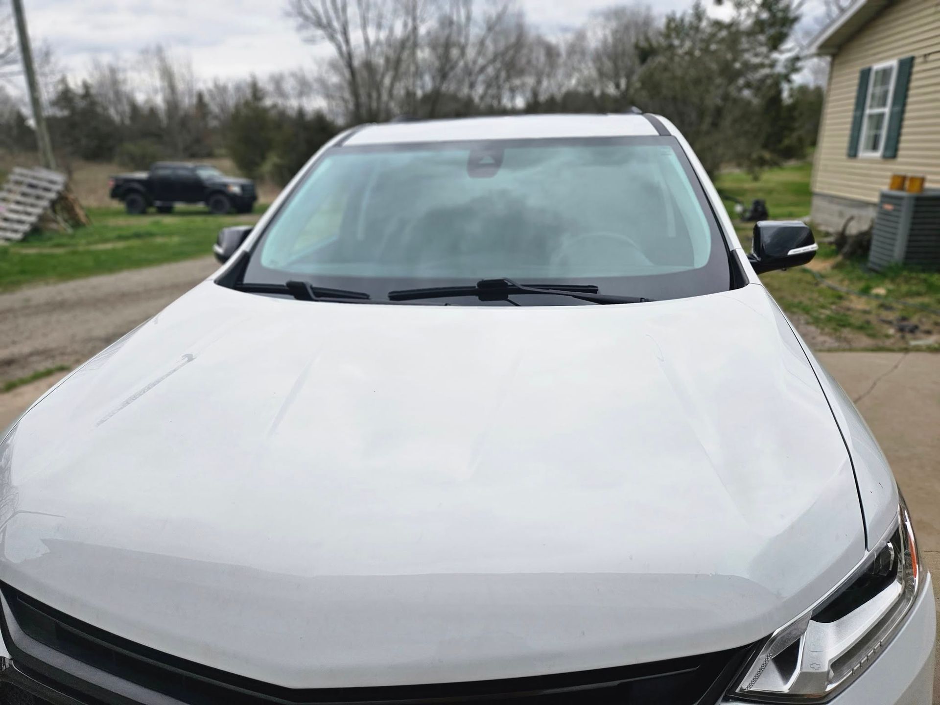 White SUV parked in front of a house on a sunny day. A truck is in the background.