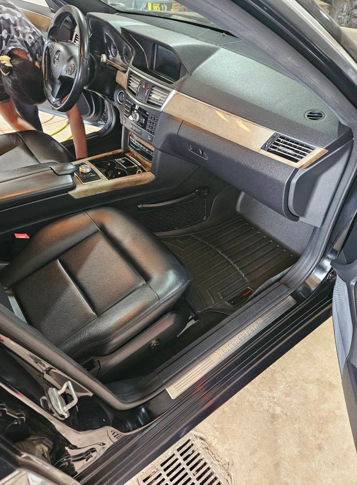 Black car interior, leather seats, dashboard, weather mats, and someone inside cleaning.
