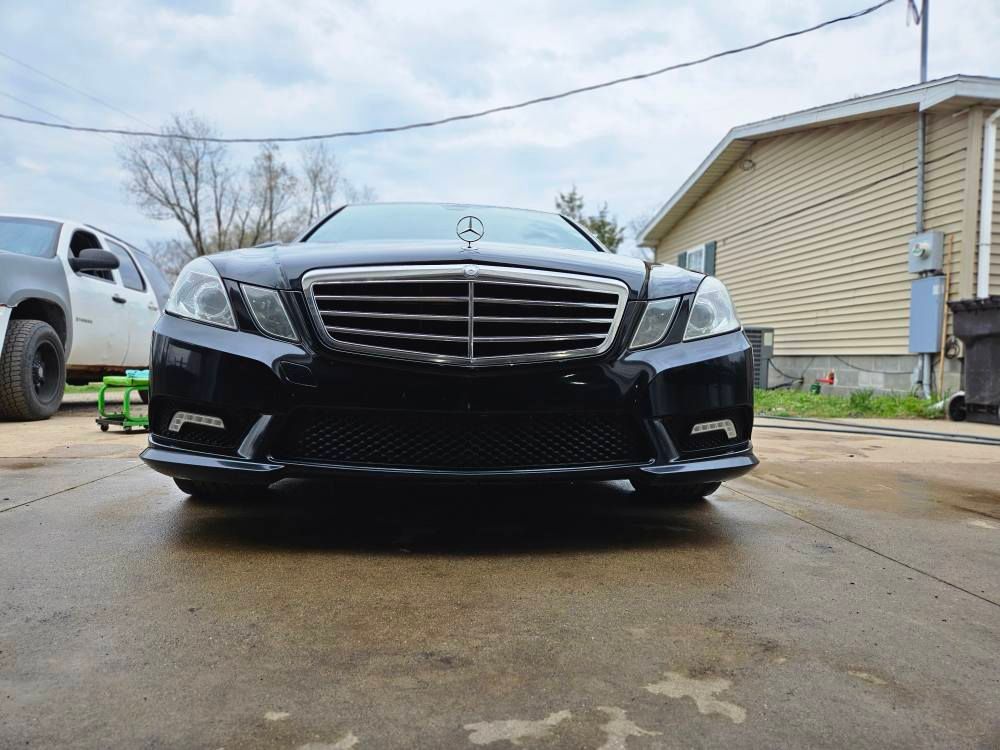 Black Mercedes-Benz sedan parked in front of a house, shot from a low angle on a wet driveway.