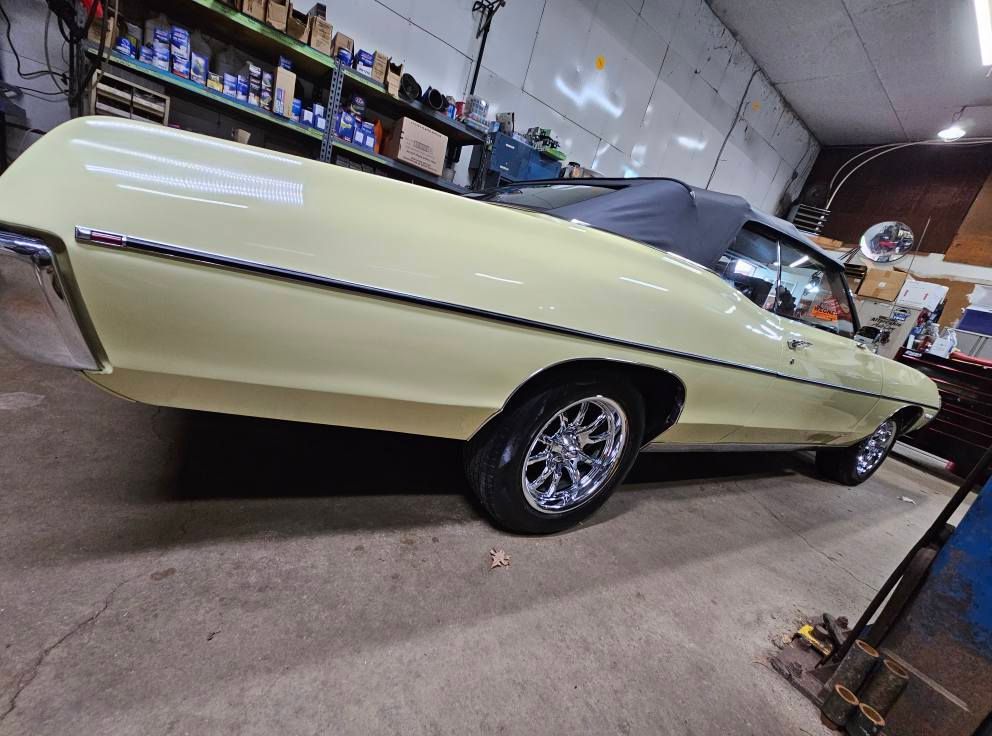 Yellow classic convertible car inside a garage, black convertible top, shiny chrome wheels.