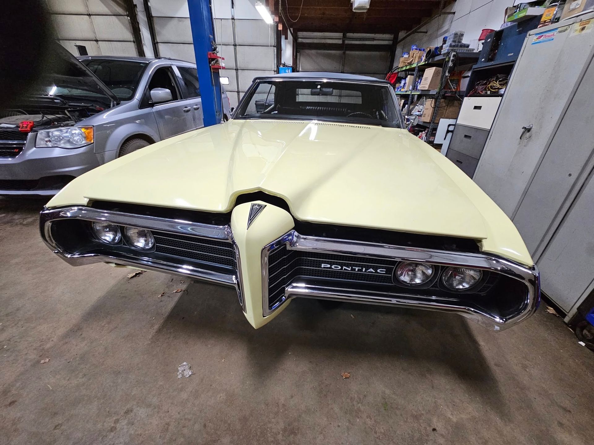 Yellow Pontiac classic car front view in a garage setting with open hood.