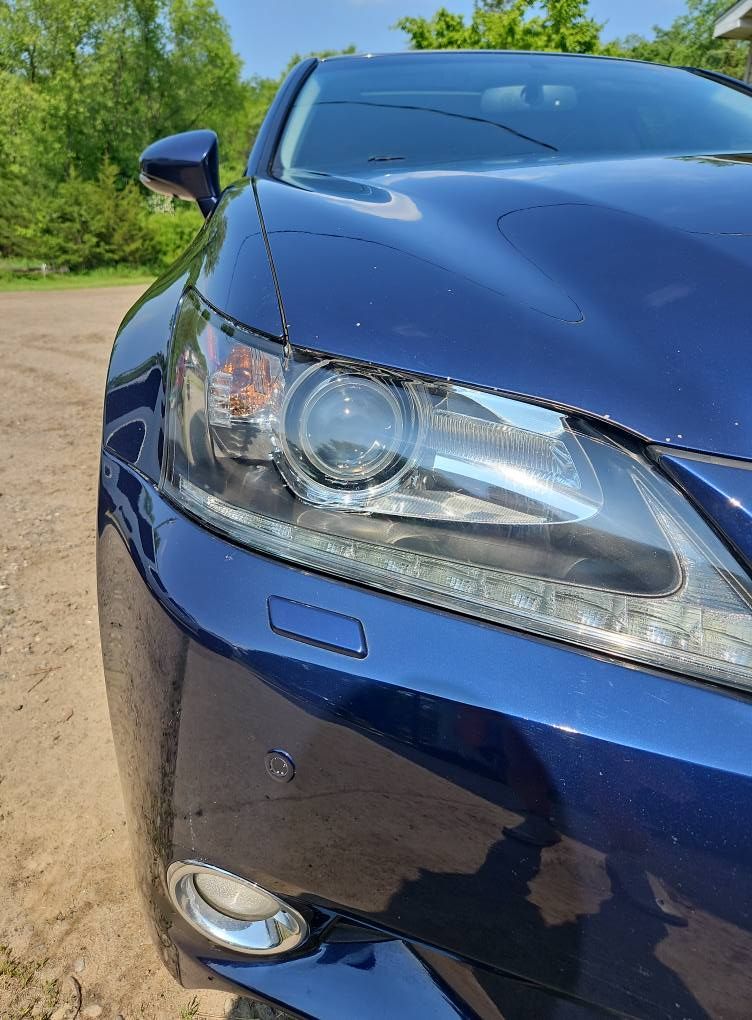Blue car's front with headlight detail. Outdoors, day.
