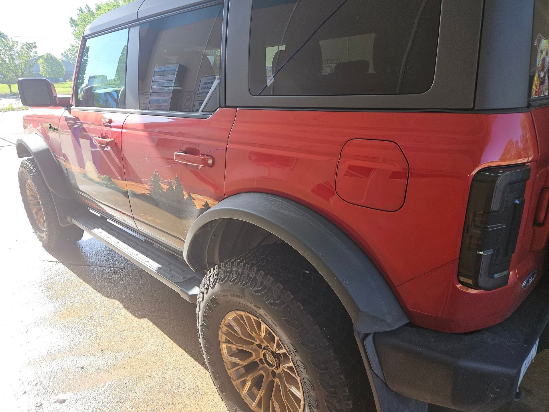 Red Ford Bronco SUV with black trim and bronze wheels, outdoors in sunlight.