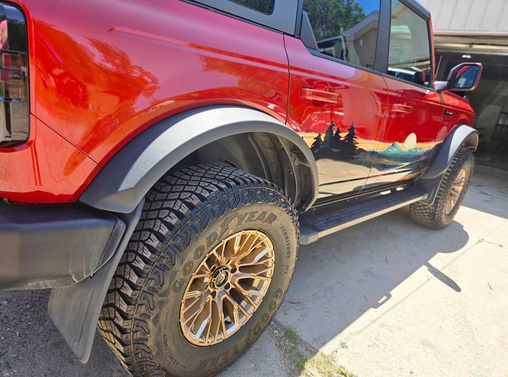Red Ford Bronco with black fender flares, bronze wheels, and a mountain landscape decal.