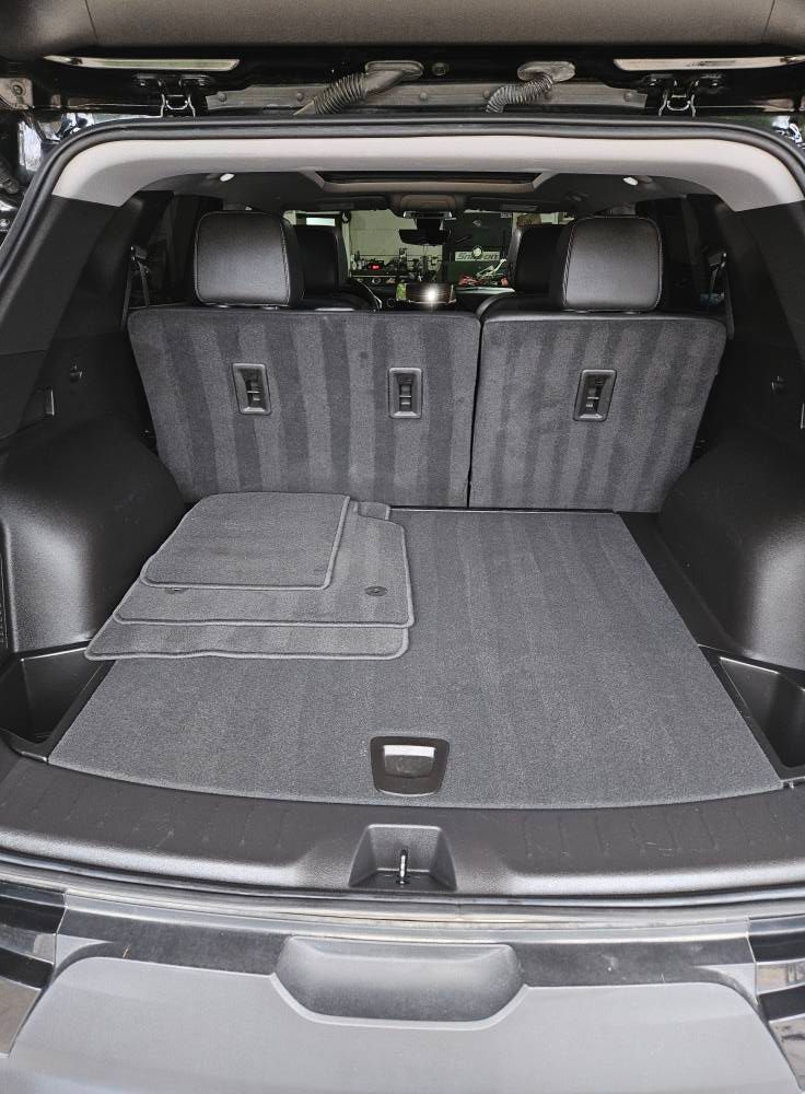Black SUV cargo area with folded seats, floor mat and carpet.