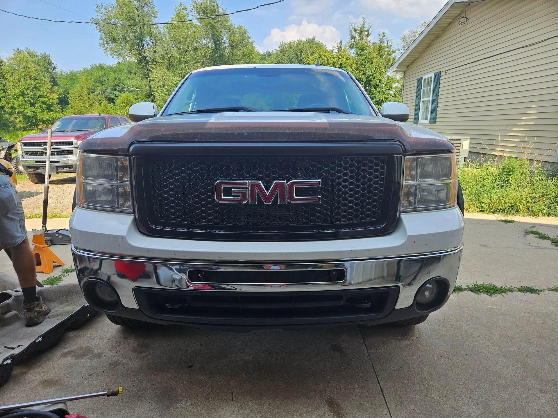 White GMC Sierra truck with a black grille and chrome bumper, parked in a driveway.