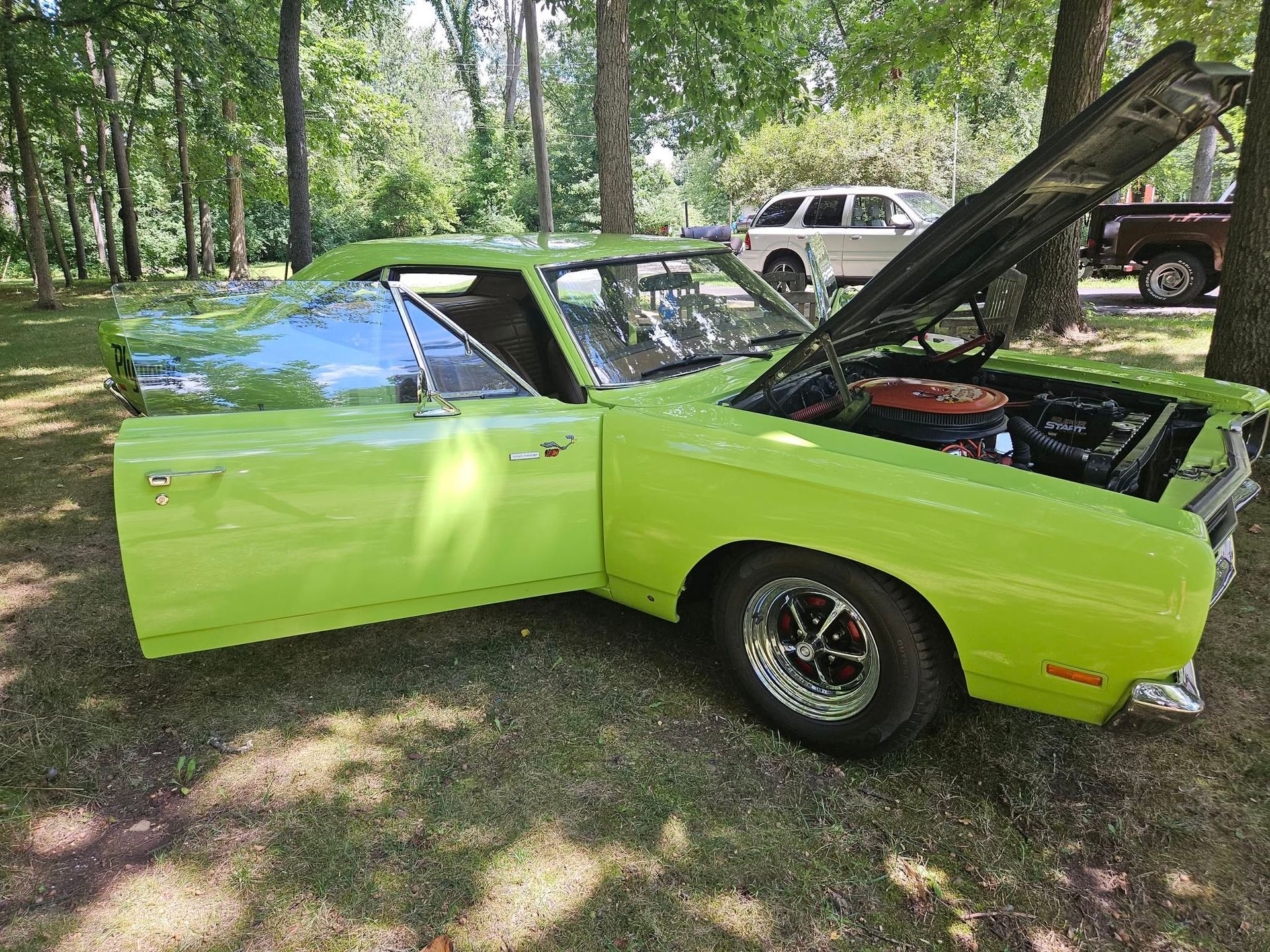 Bright green classic Dodge muscle car with open hood and door parked on grass.