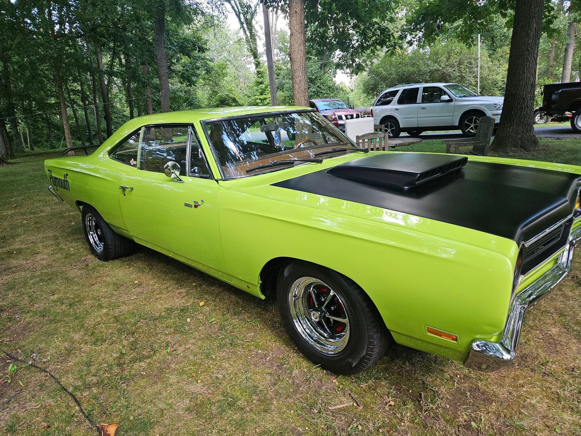 Green classic Plymouth Road Runner car on grass, black hood scoop, parked outdoors.