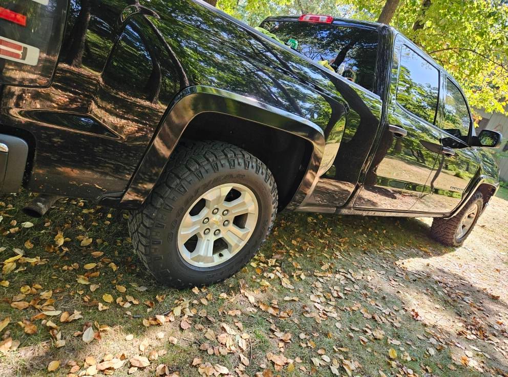 Black pickup truck parked on grass, tires visible, surrounded by fall leaves.