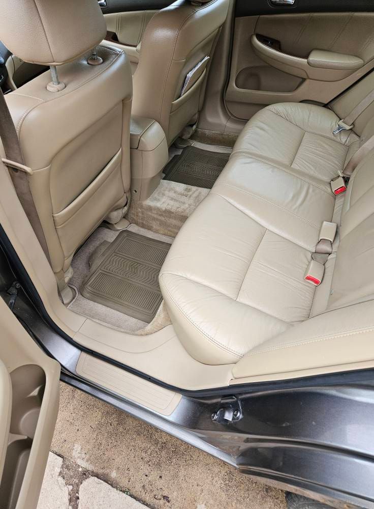 Beige leather car backseat with seatbelts, floor mats, and door frame visible.