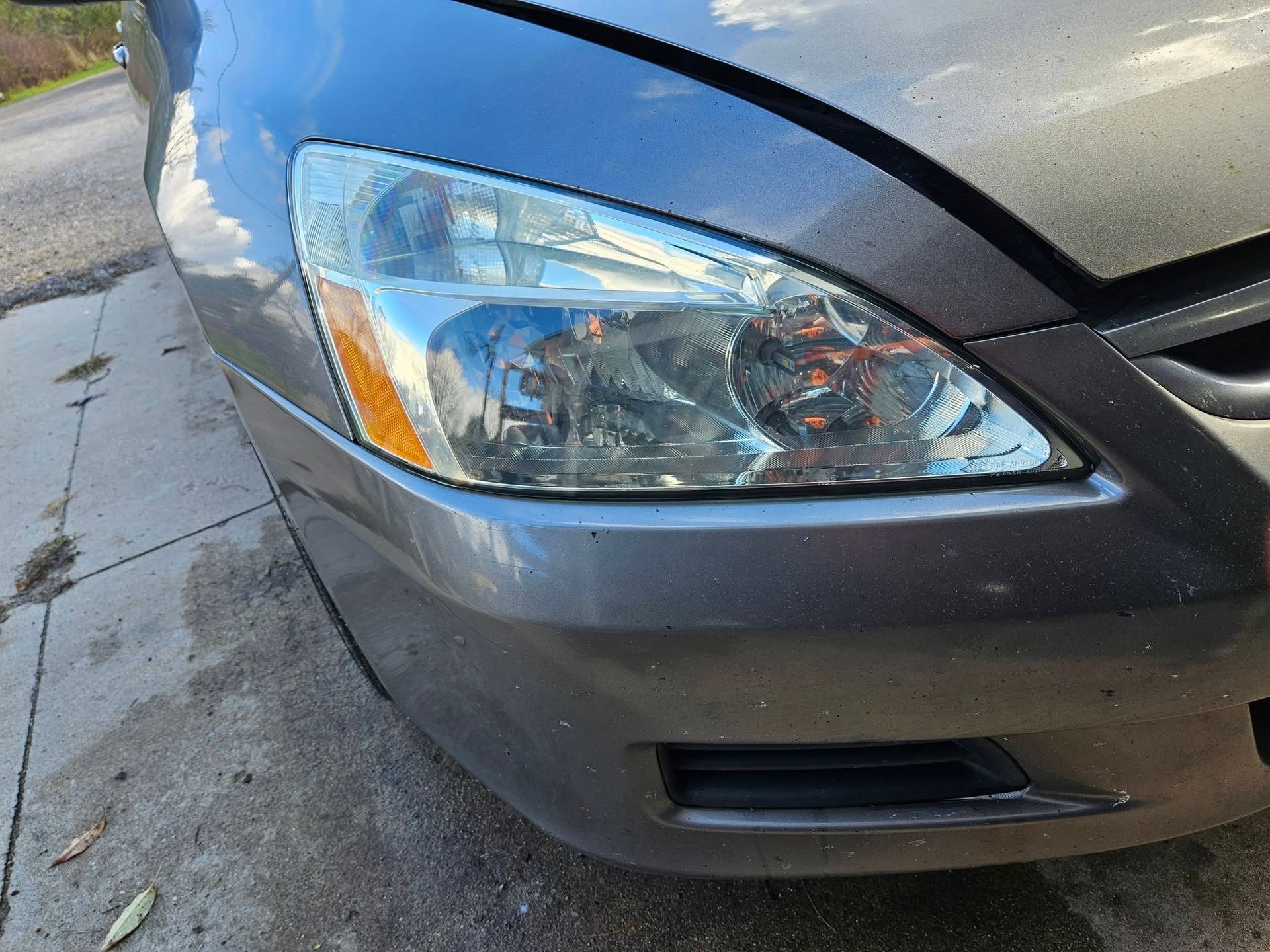Gray car headlight and front bumper on a driveway.