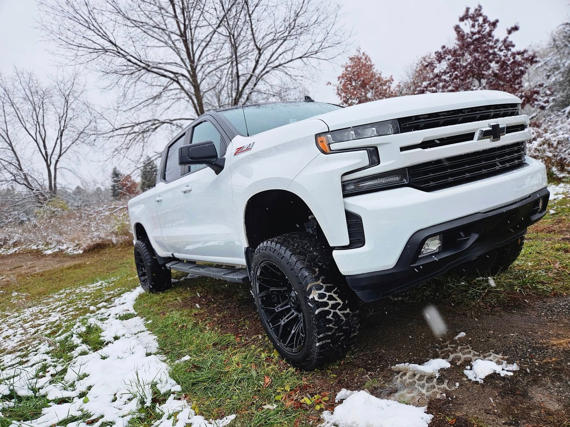 White Chevrolet Silverado truck with black wheels on a snowy trail.