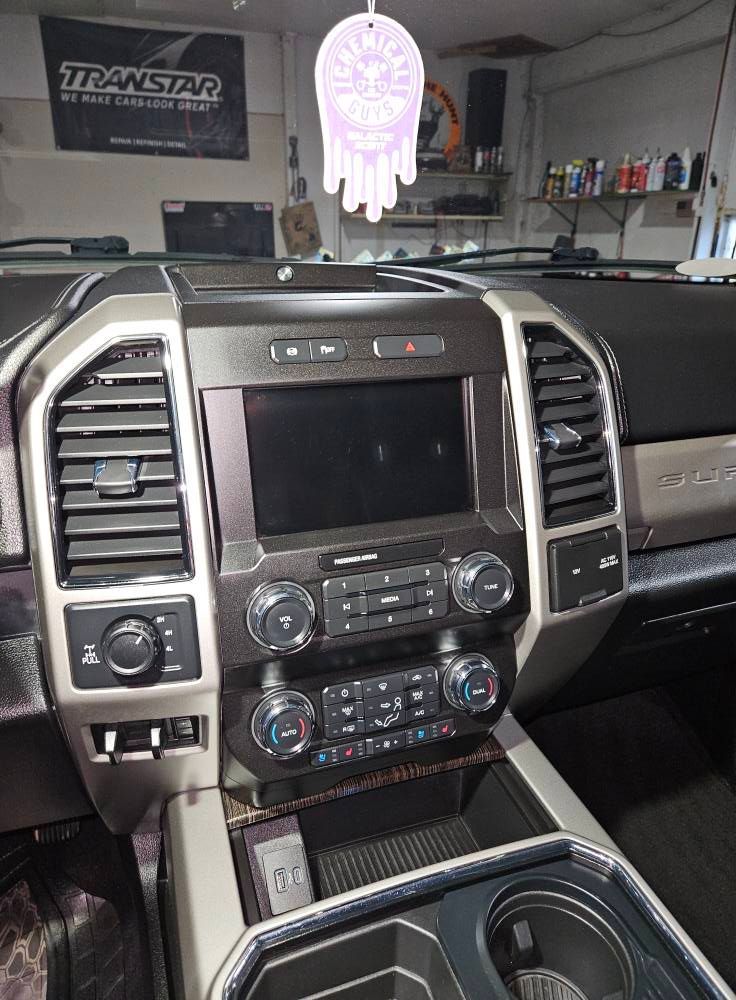Interior of a vehicle dashboard with a large central screen, air vents, and control knobs.