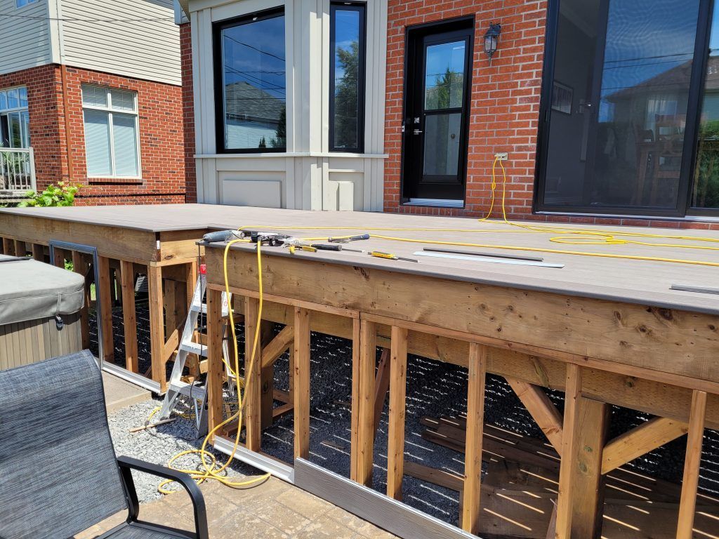 Une terrasse en bois est en cours de construction devant une maison en briques.