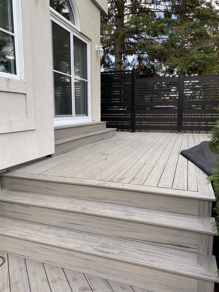 Une terrasse en bois avec des escaliers qui y mènent à côté d'une maison.