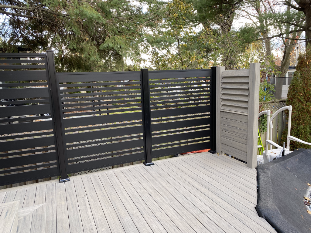 Une clôture noire entoure une terrasse en bois avec des arbres en arrière-plan.