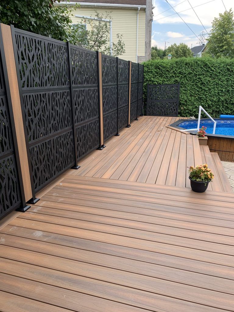 Une terrasse en bois avec une clôture et une piscine en arrière-plan.